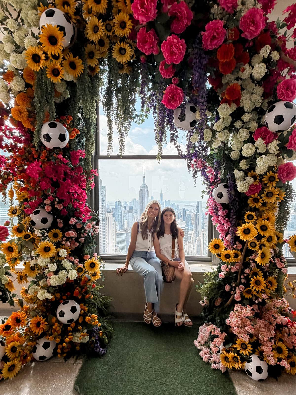 Mom and tween daughter at Top of the Rock with a beautiful flower arch and Empire State Building skyline view in New York City