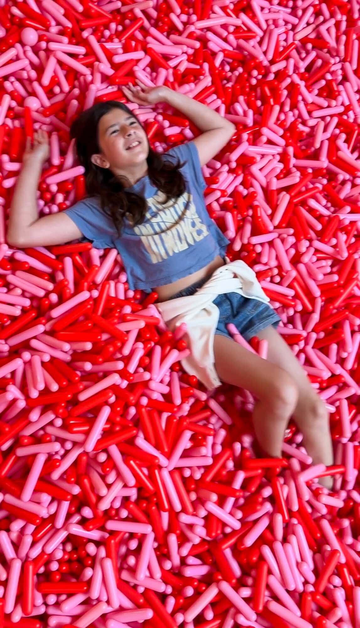 Tween daughter lying in a pile of red sprinkles at the Museum of Ice Cream NYC