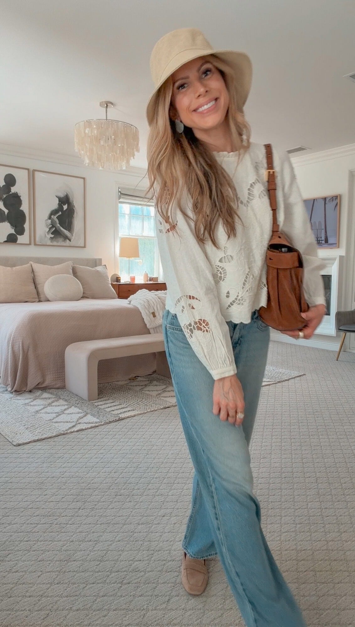Corrine in a floral cutwork linen blouse and bucket hat with low-rise jeans and a suede bag