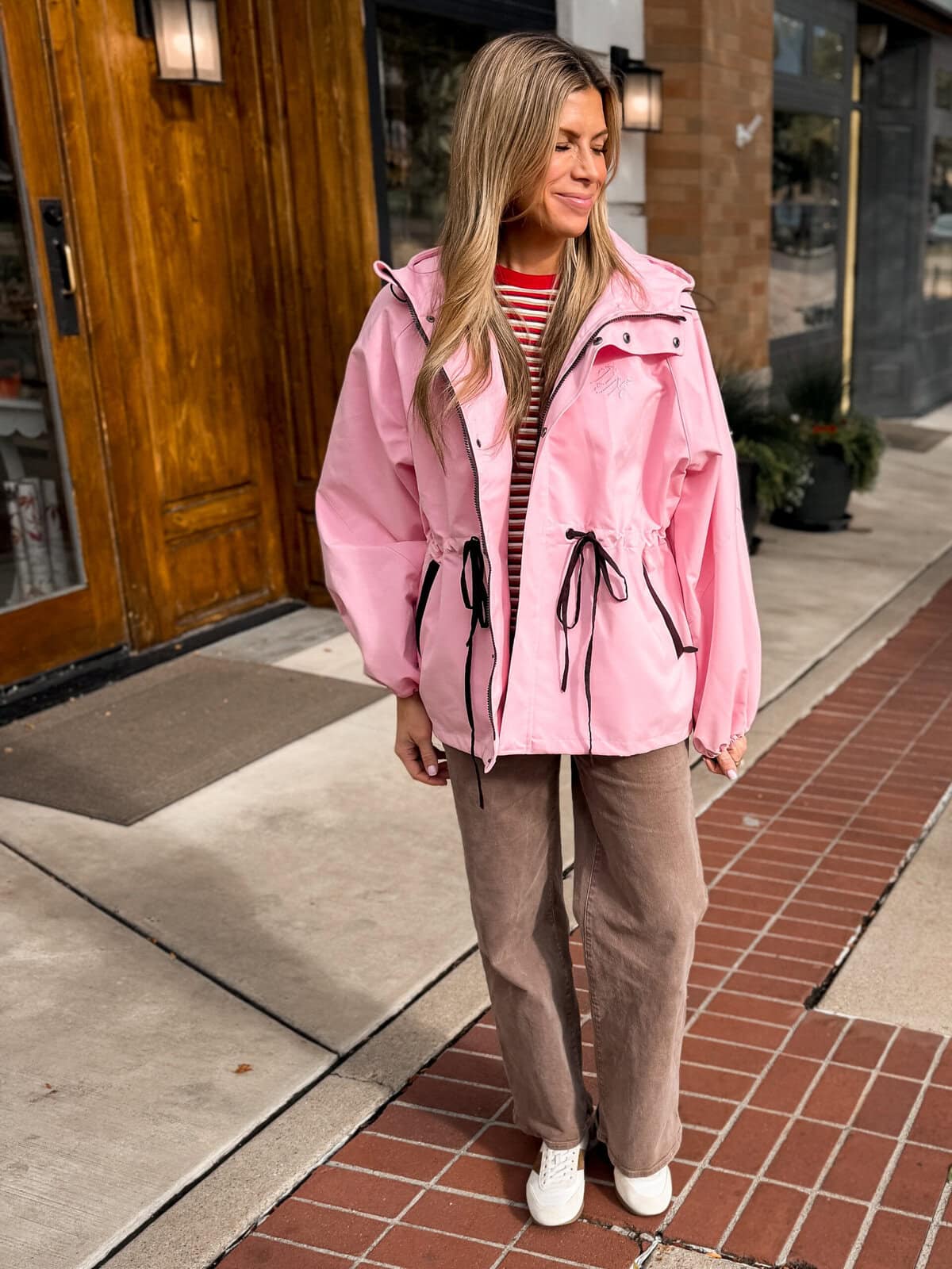 Pink raincoat with drawstring waist styled with brown wide leg jeans and sneakers