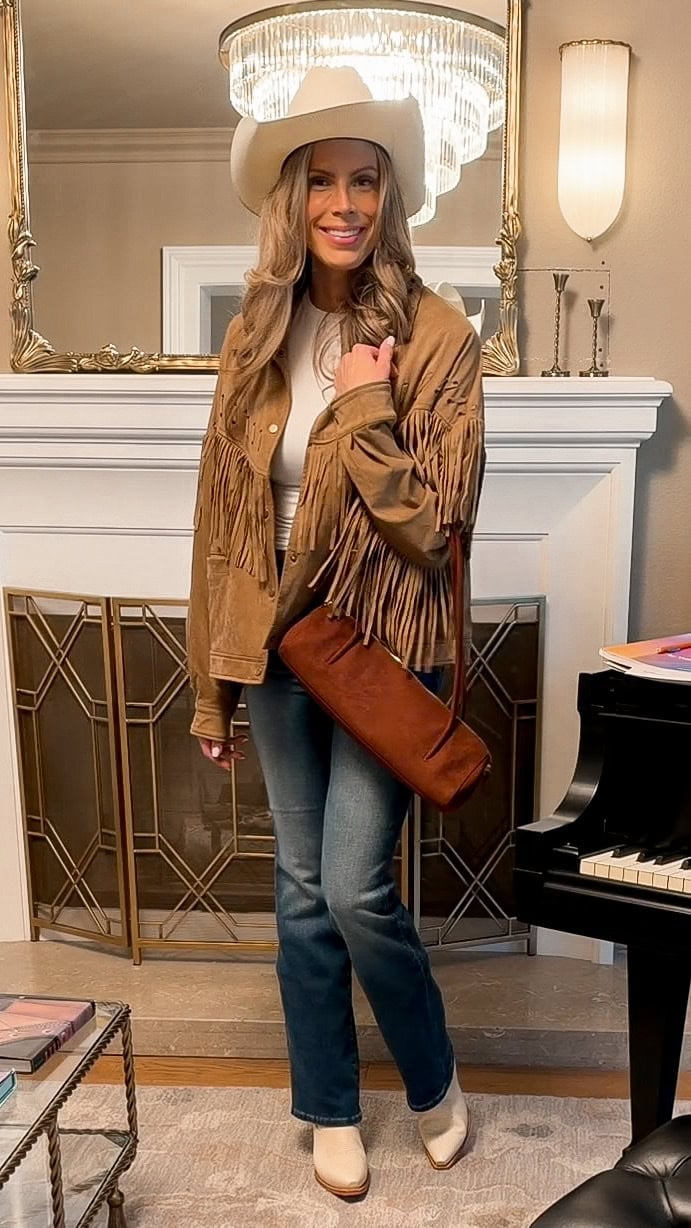 Bootcut jeans worn over cream cowboy boots with a brown fringe jacket and cowboy hat