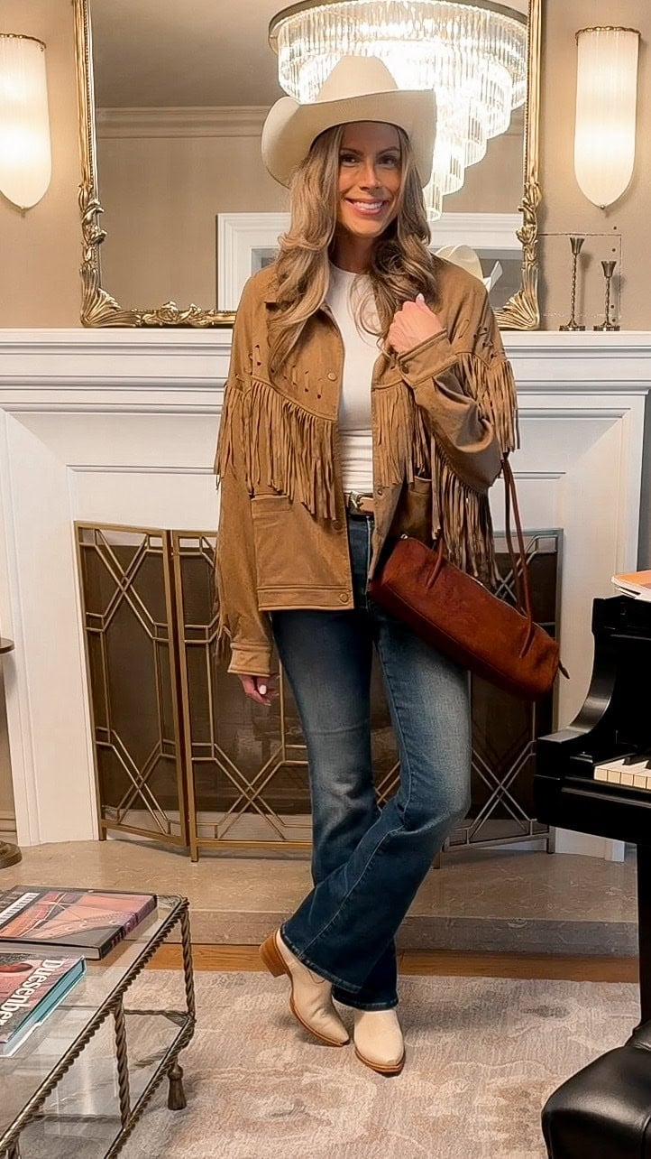 Corrine Stokoe in a brown fringe faux suede jacket, white long sleeve tee, bootcut jeans, cream cowboy boots and a cream cowboy hat, holding a brown East-West bag
